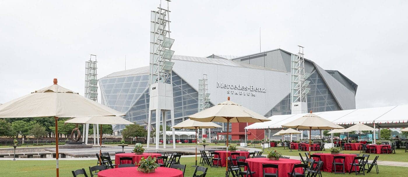 Installation pour un événement en plein air réalisée par WM Events, avec des tables rouges et noires, des parasols et des tentes à l'extérieur du Mercedes-Benz Stadium, par temps nuageux.